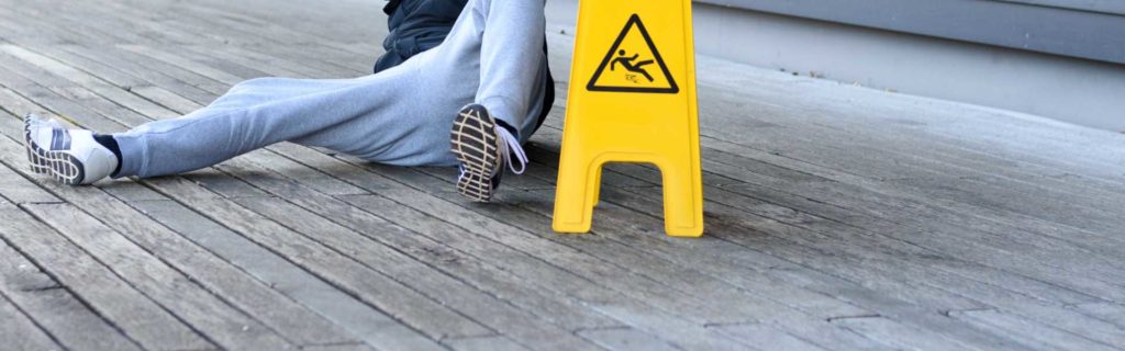 A person on the ground near a warning sign after a slip and fall accident