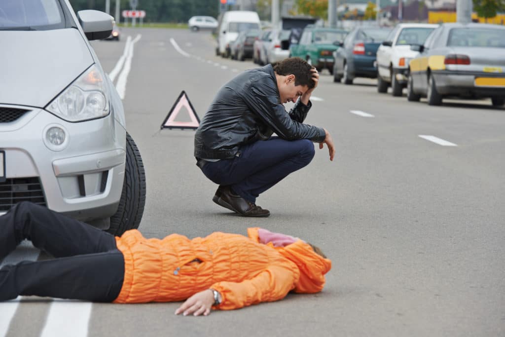 An upset driver kneels near an injured person on the roadway after a car accident