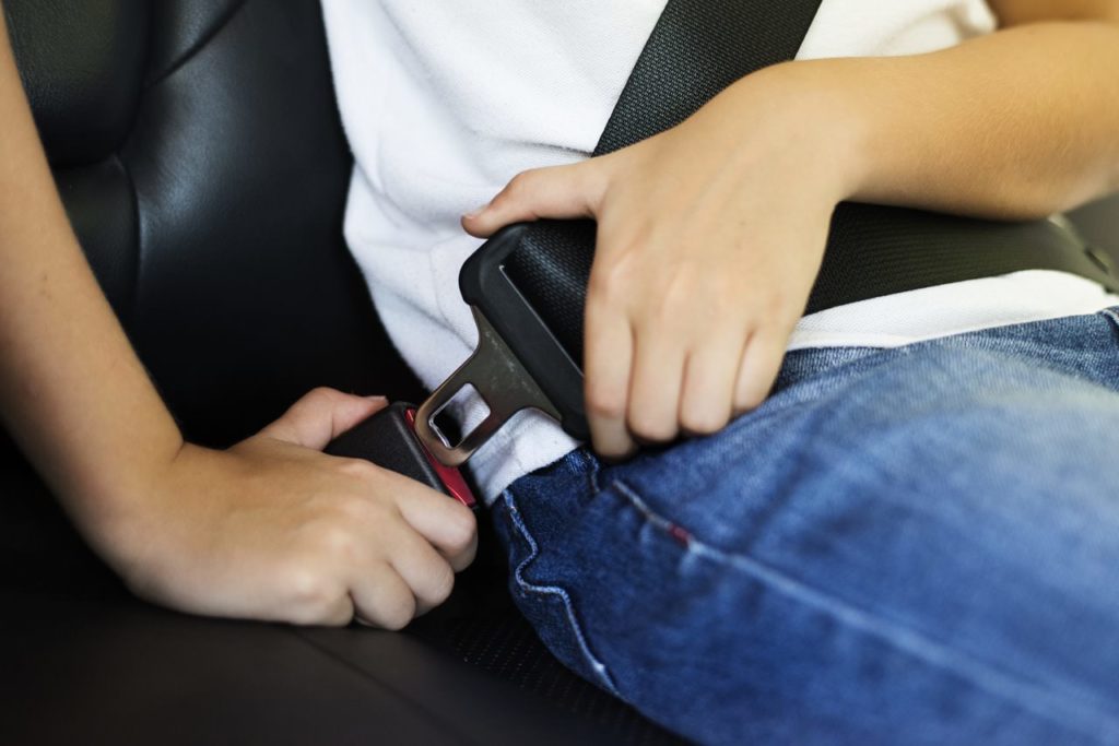 Child buckling a seat belt to help prevent injuries in case of a car accident