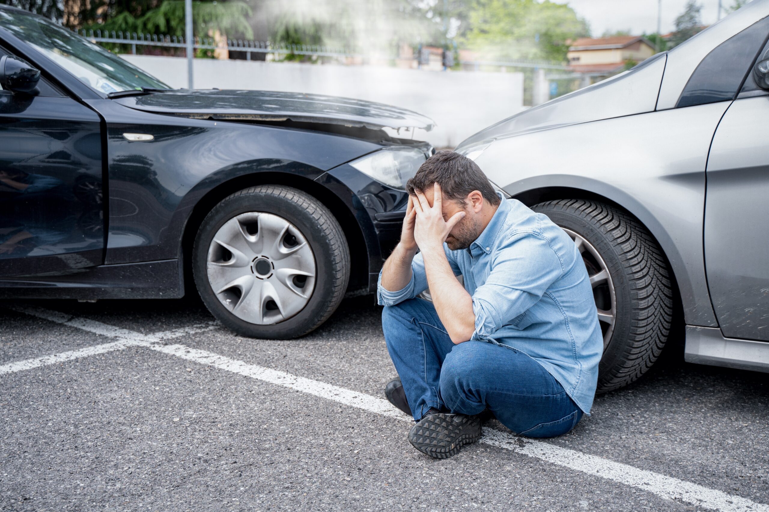 man sitting on the ground with head in his hands after a car accident between two cars