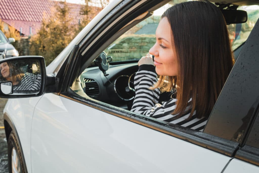 Woman leaning on the window of a white car, looking outside in a residential area.