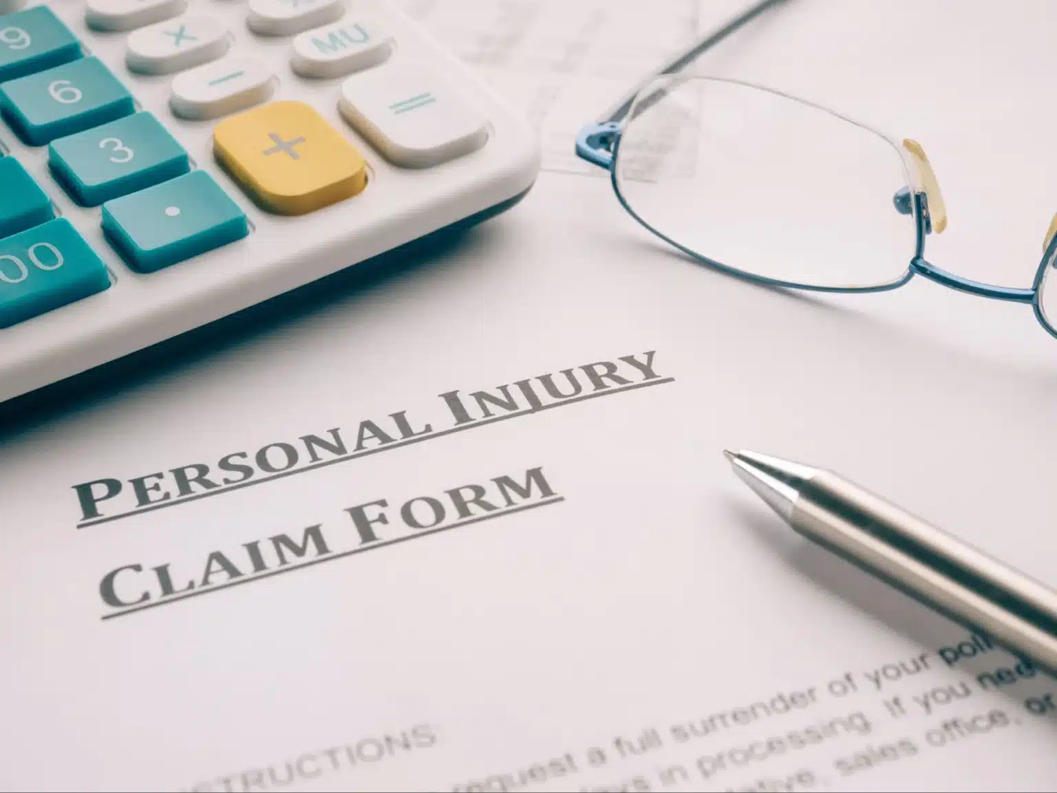 Personal injury claim form with calculator, pen, and glasses on desk.