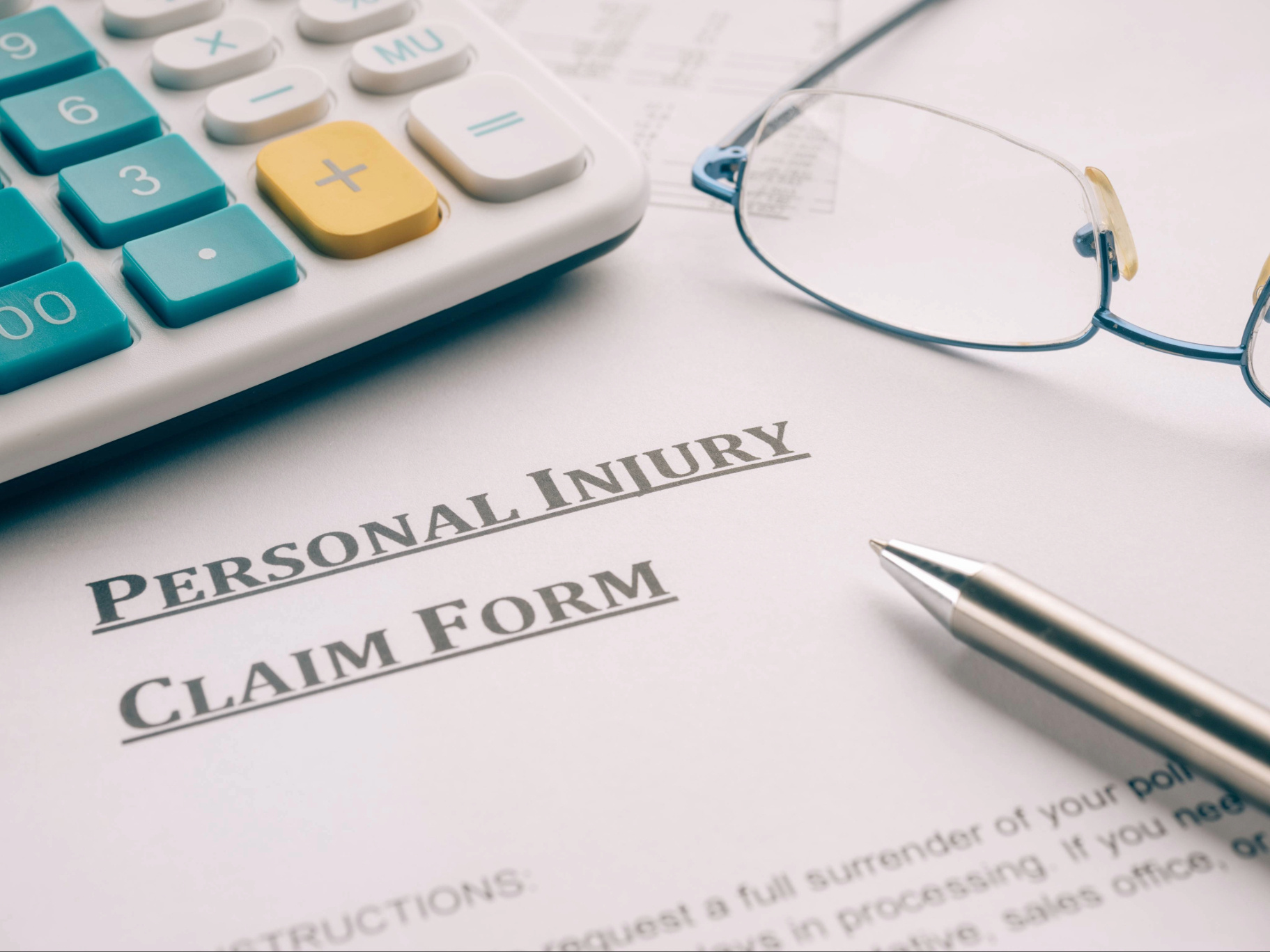 Personal injury claim form with calculator, pen, and glasses on desk.