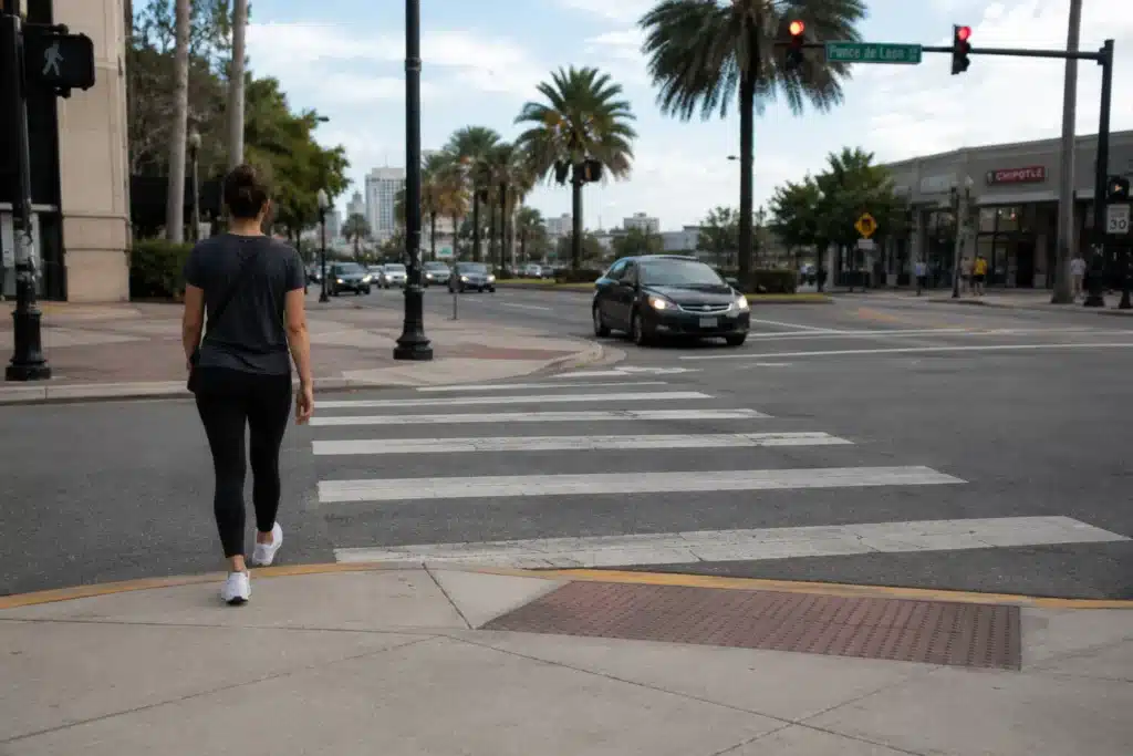 Peatón cruzando una calle de Miami por un paso de peatones señalizado cerca del bulevar Ponce de León, con palmeras y el horizonte del centro de la ciudad de fondo