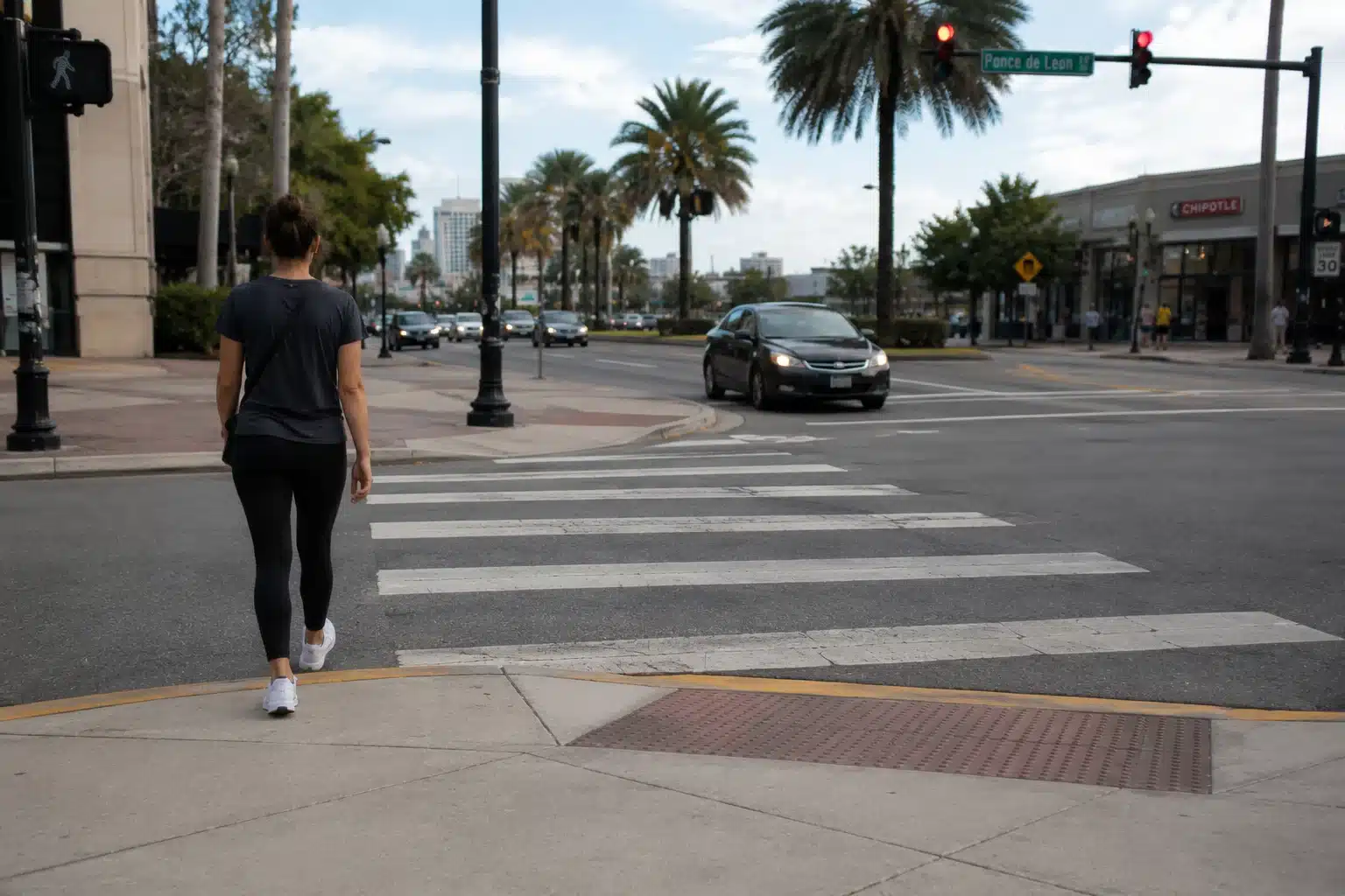 Peatón cruzando una calle de Miami por un paso de peatones señalizado cerca del bulevar Ponce de León, con palmeras y el horizonte del centro de la ciudad de fondo